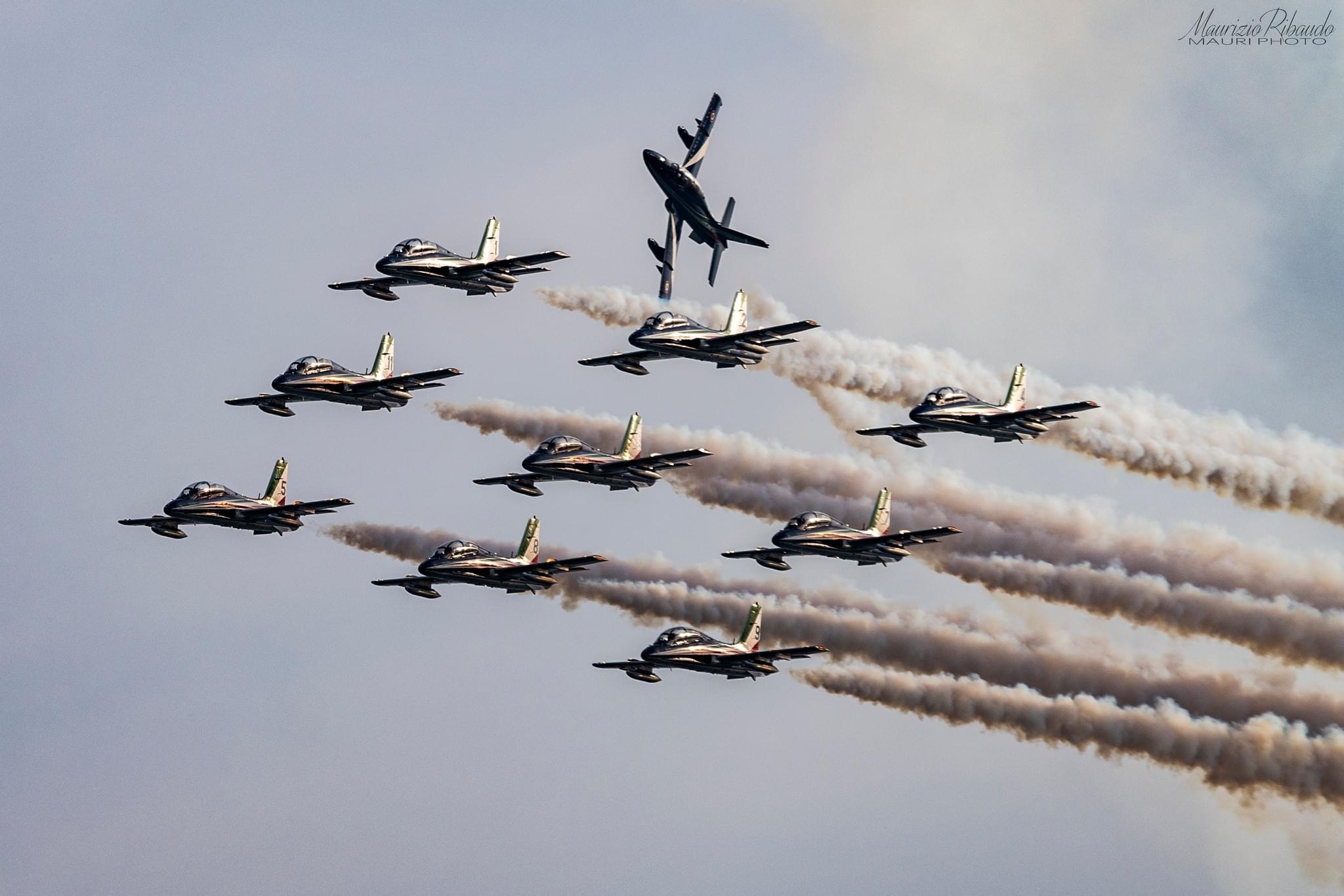 Aerobatic jets flying toward the right with smoke trails in a horizontally mirrored photograph — credited to Maurizio Ribaudo / Mauri Photo