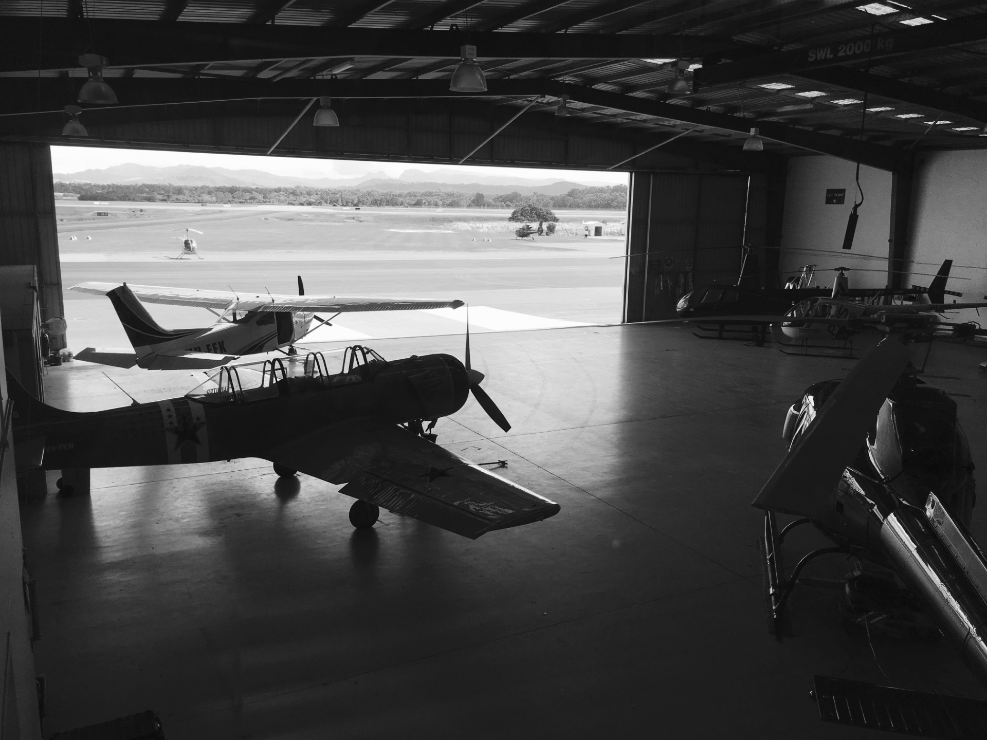 Black-and-white photograph of vintage aircraft and helicopters inside a hangar