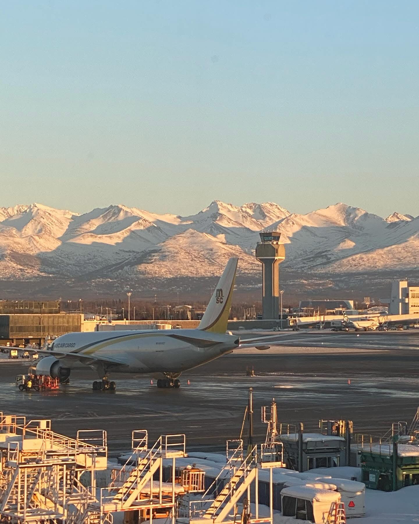 An airport apron and control tower beneath snow-covered mountains
