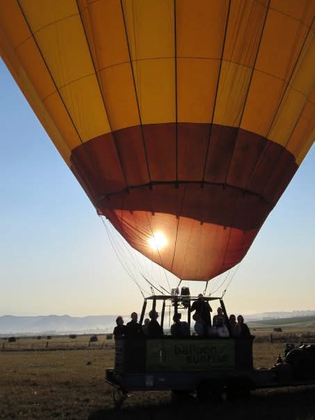 Passengers beneath a hot-air balloon as its burner glows before liftoff