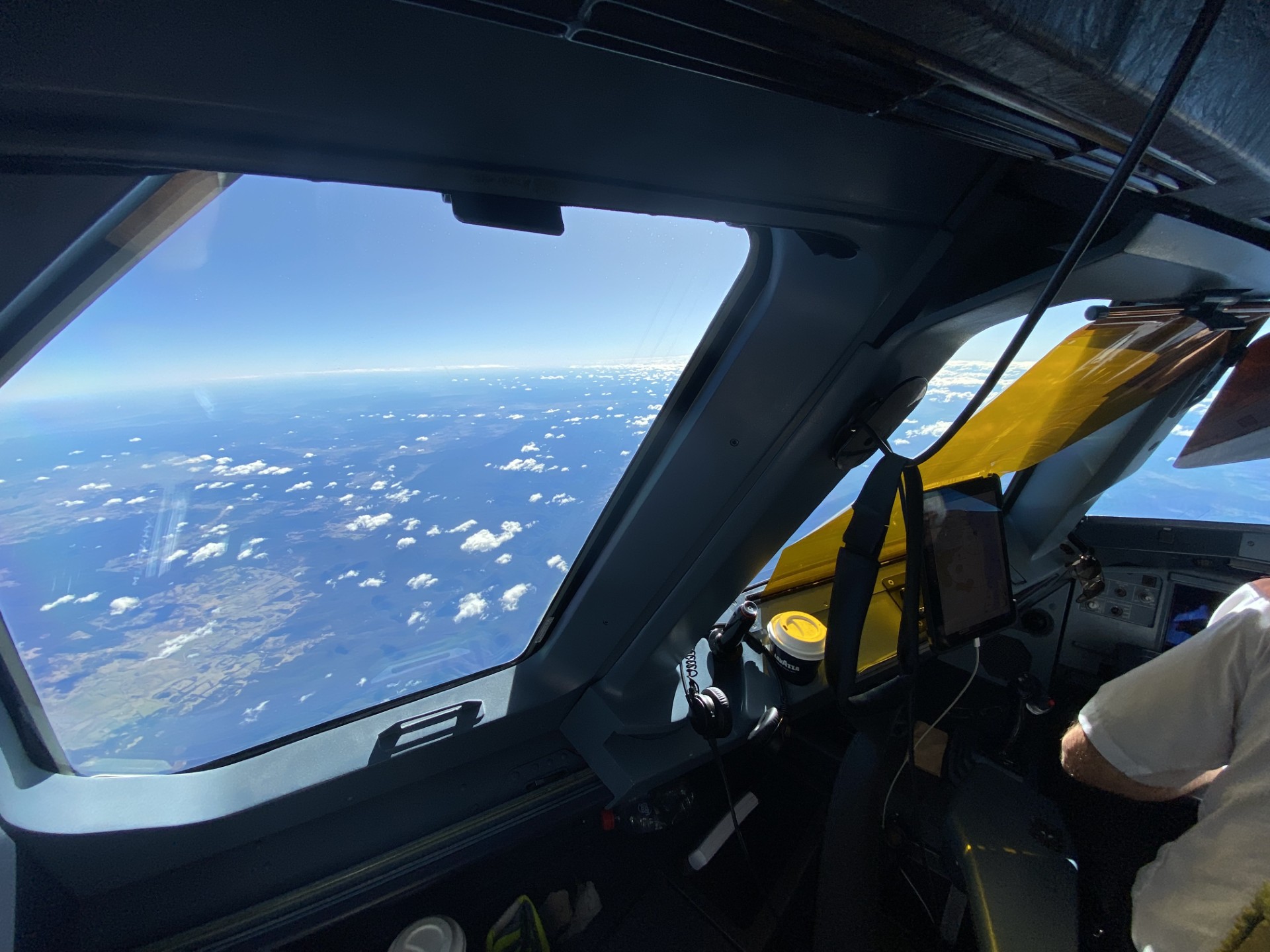 Scattered clouds and the landscape below seen through a flight-deck window