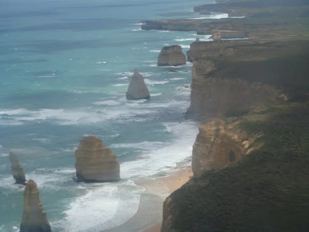 Ocean waves and rock stacks beside coastal cliffs, seen from the air