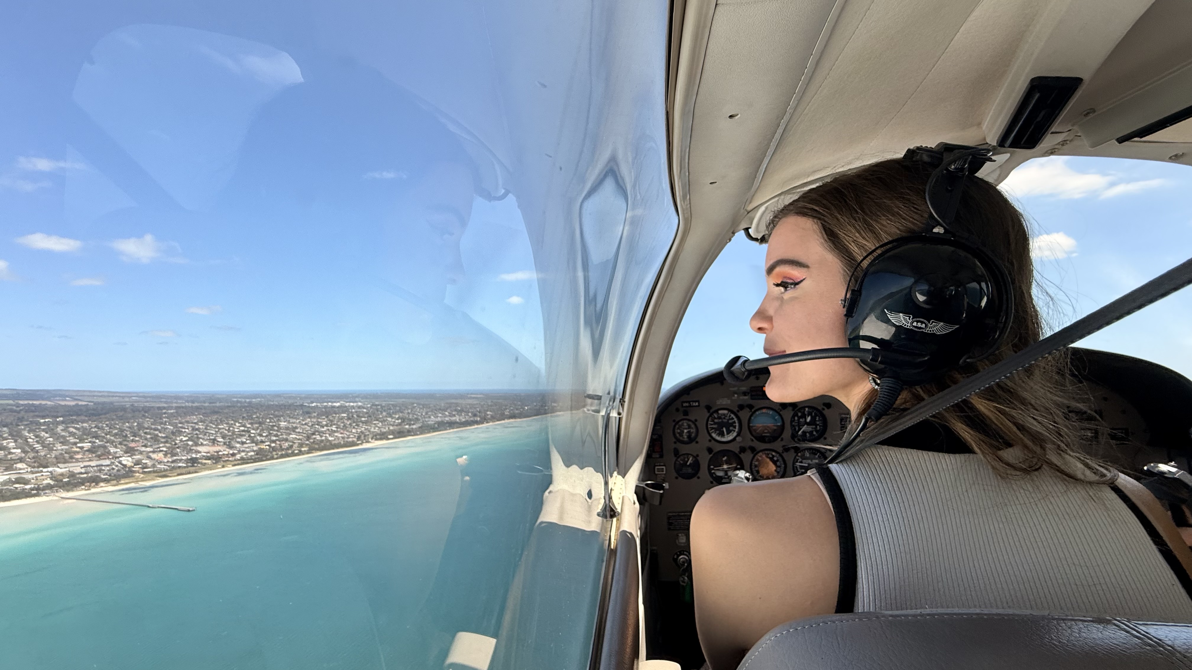 A headset-wearing passenger looking out over a coastline during a light-aircraft flight