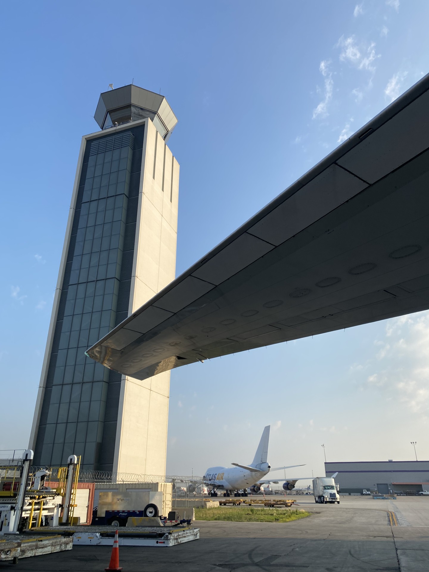 An airport control tower framed by the underside of an aircraft wing