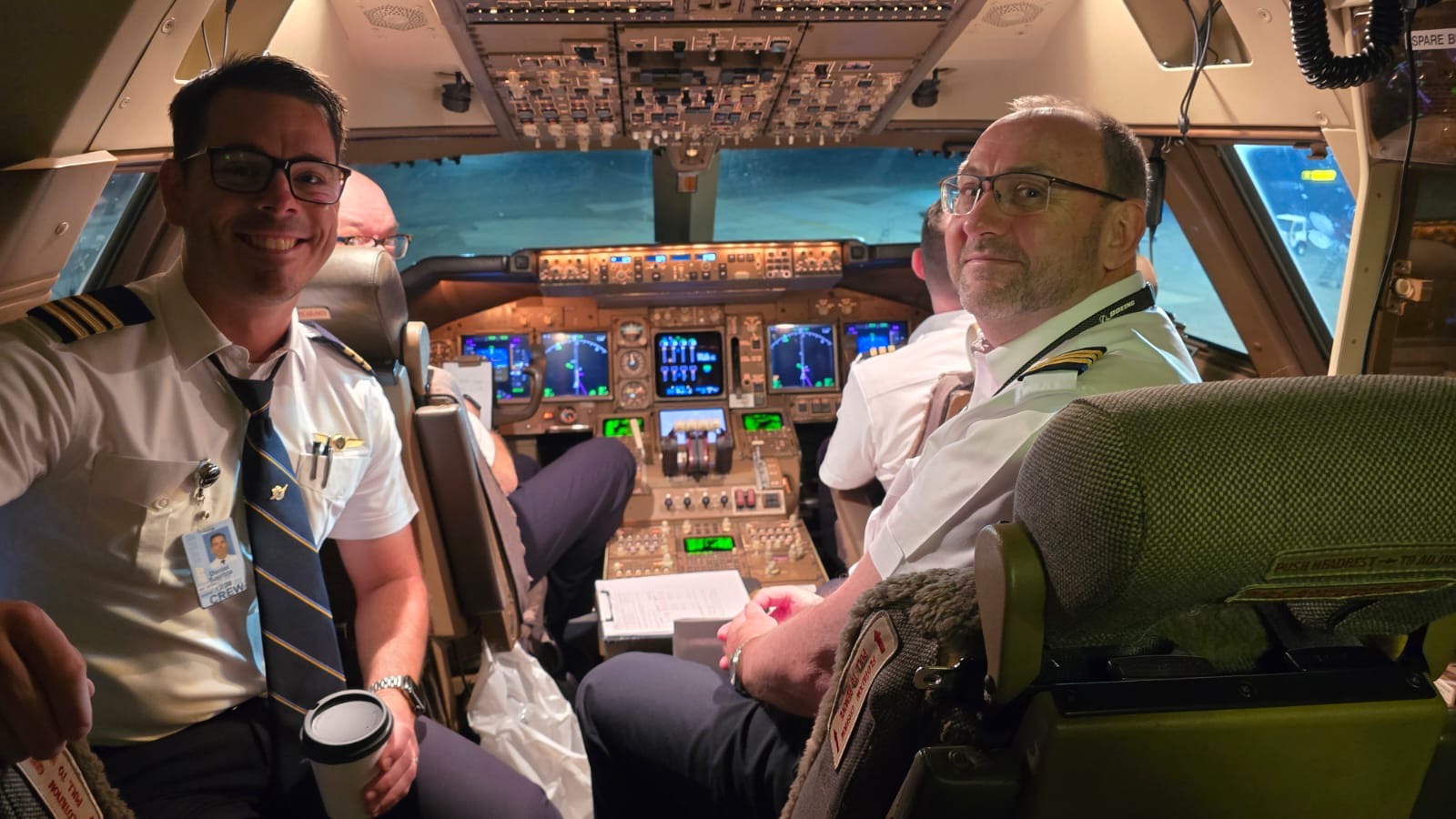Two pilots smiling together on an illuminated airliner flight deck