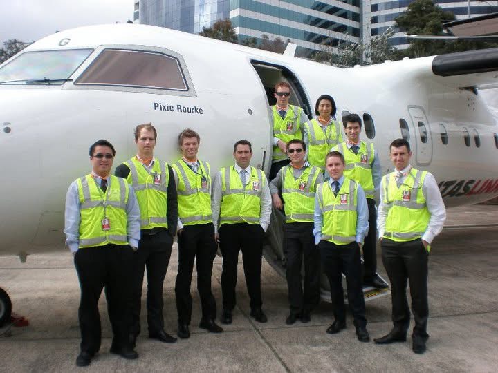 An aviation crew in high-visibility jackets gathered beside a turboprop