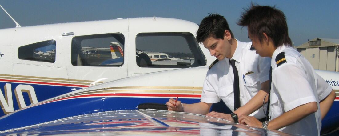 Two pilots planning a flight together on the wing of a training aircraft