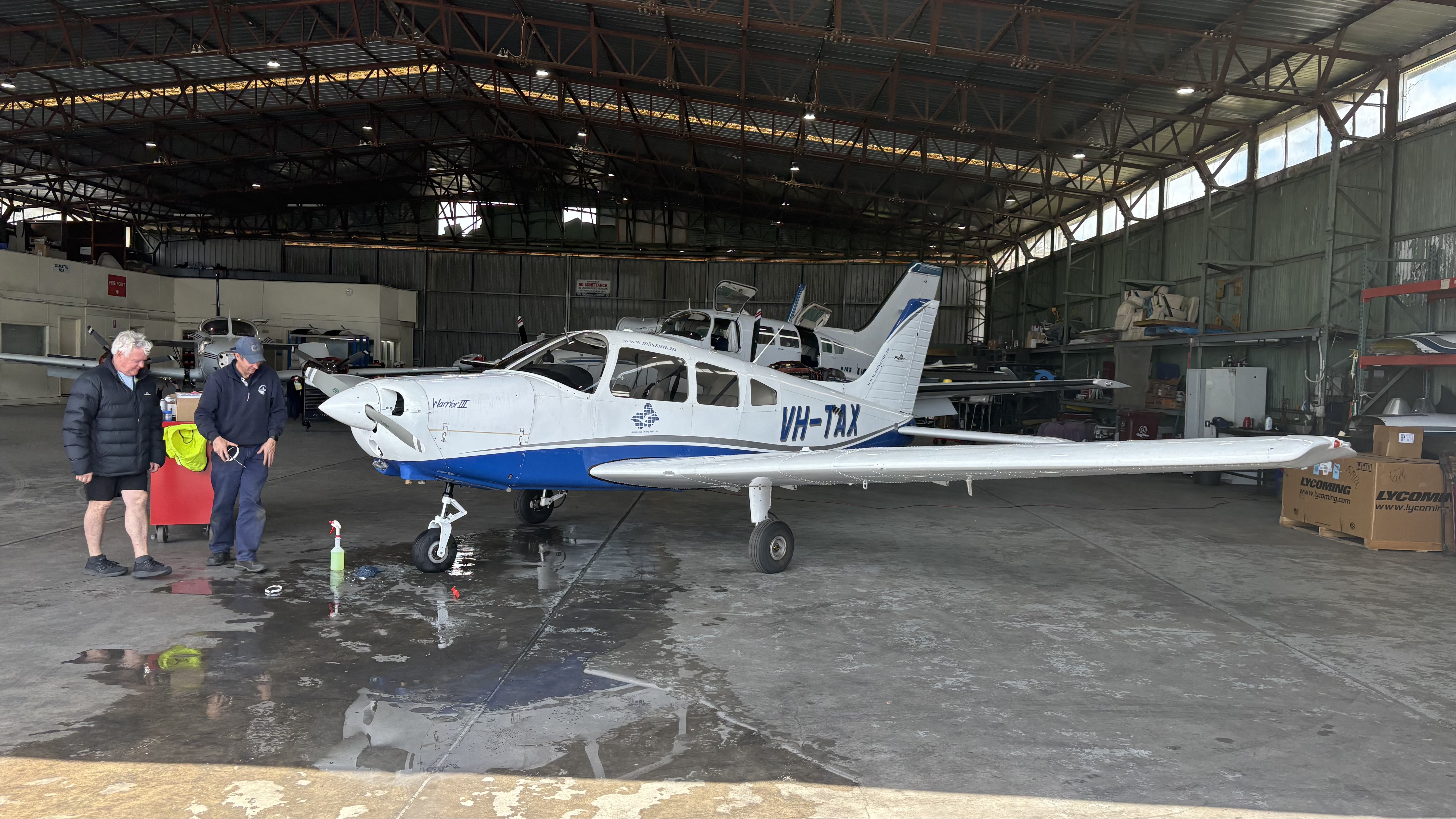 A light aircraft parked inside a hangar with visitors nearby