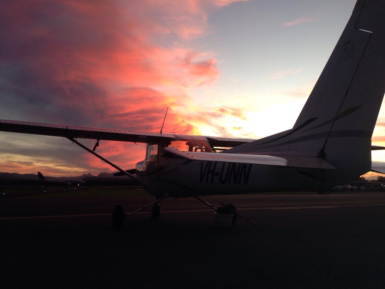A high-wing light aircraft silhouetted against clouds at sunset