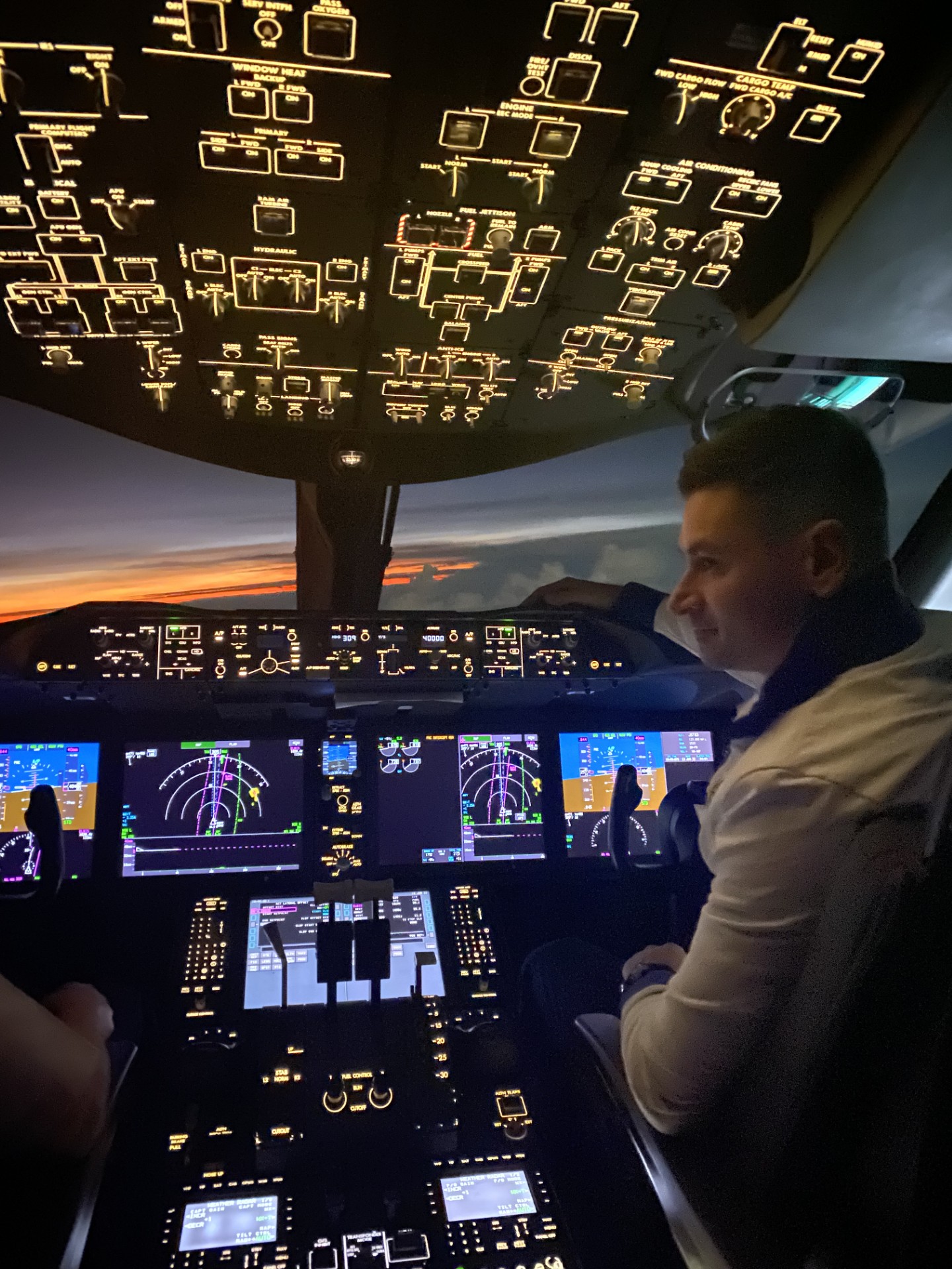 A pilot at the controls beneath the illuminated overhead panel at sunset