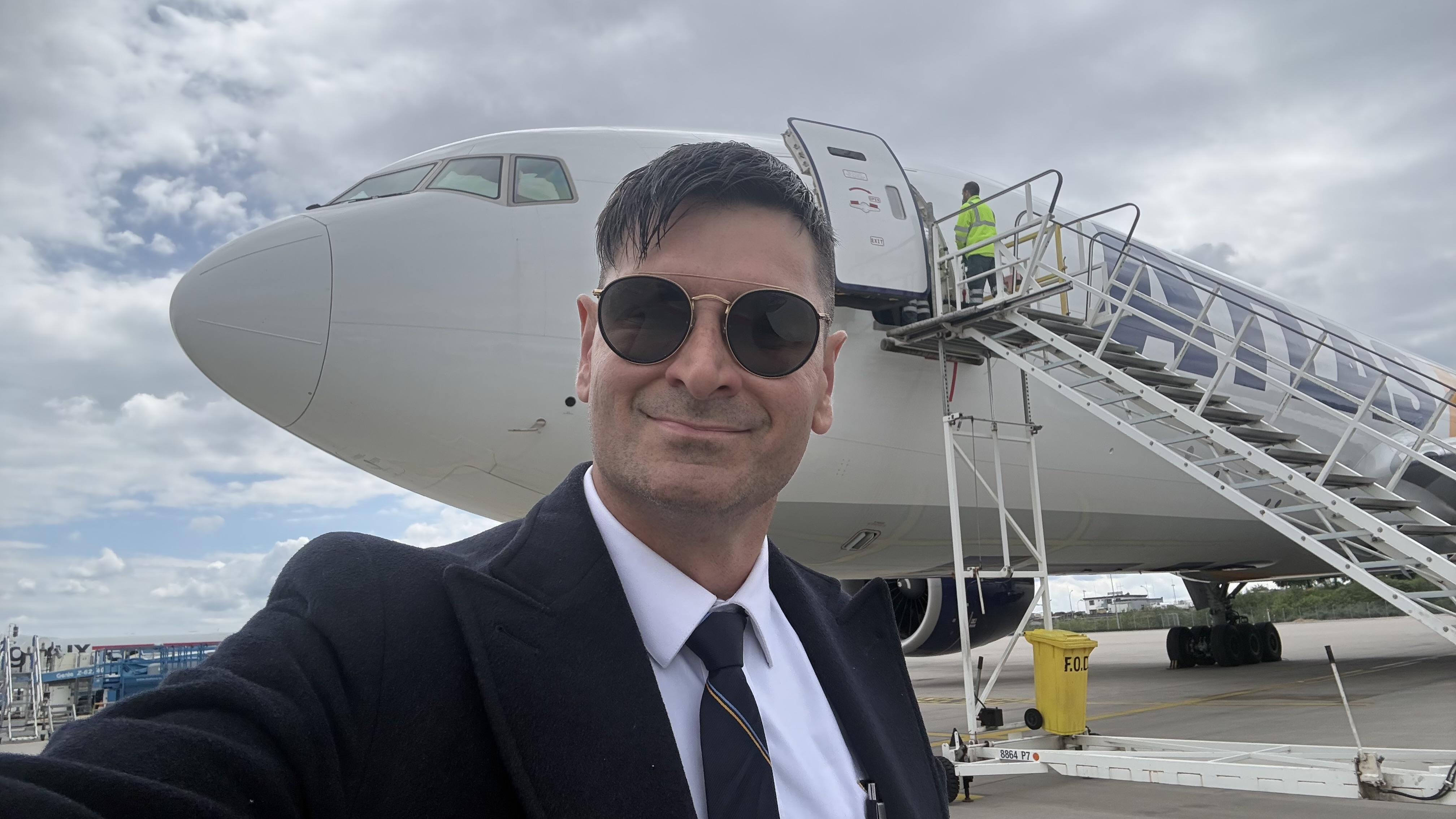A pilot in uniform beside an airliner and its boarding stairs