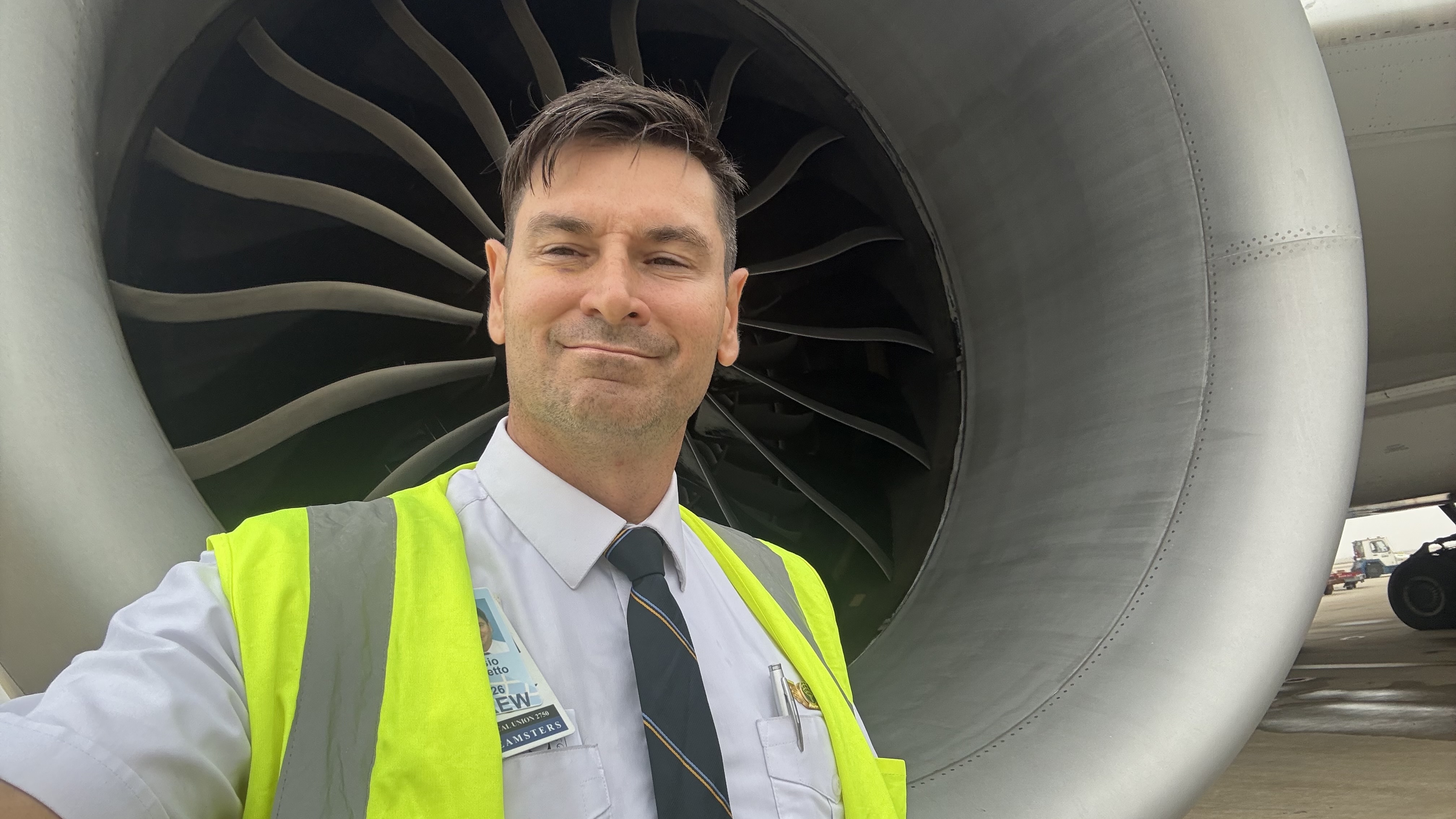 A pilot in a high-visibility vest beside a large jet engine
