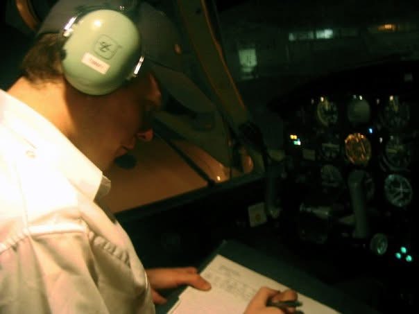 A pilot wearing a headset and making notes beside the cockpit instruments