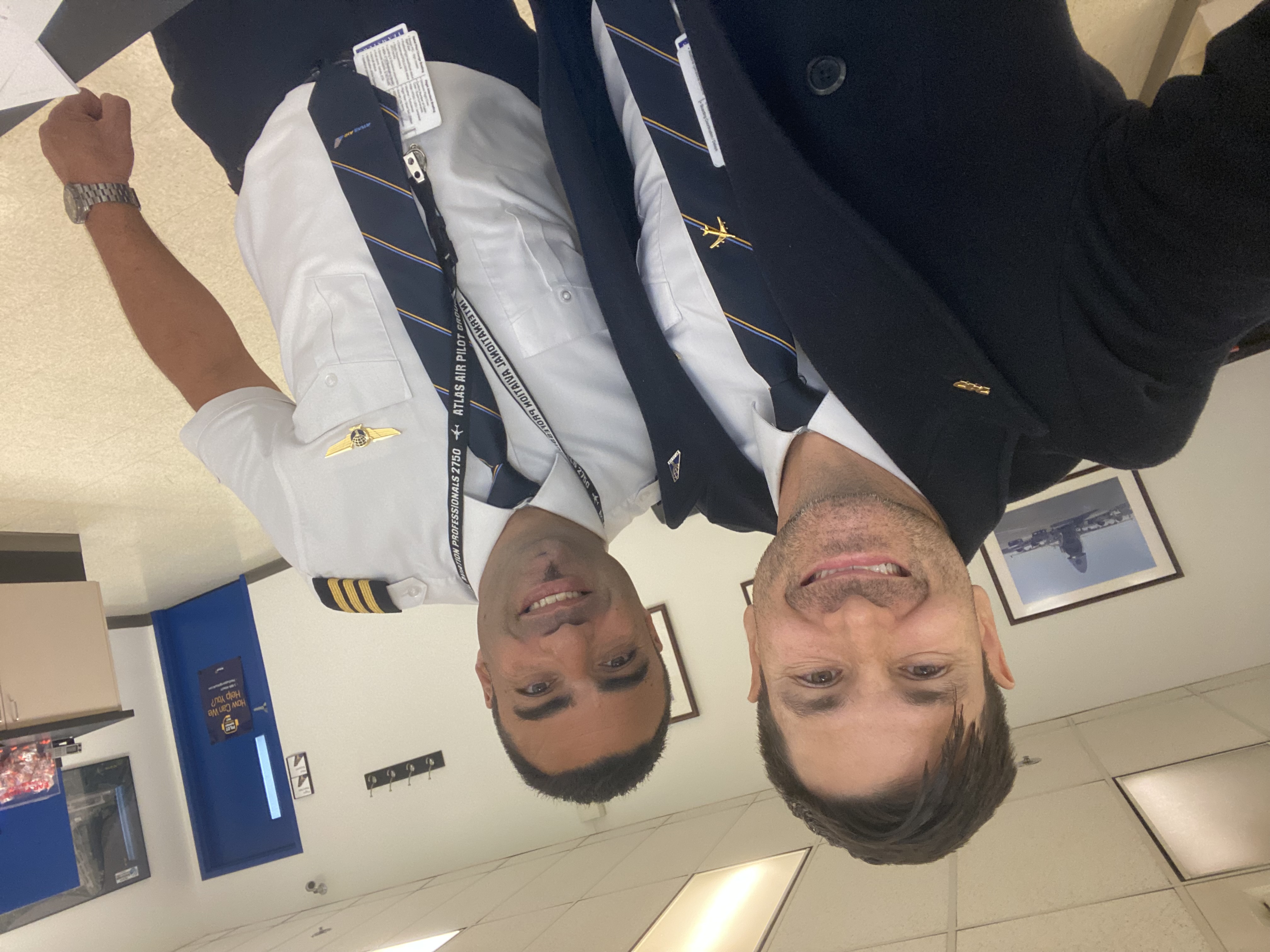 Two pilots in uniform smiling together inside an airport building