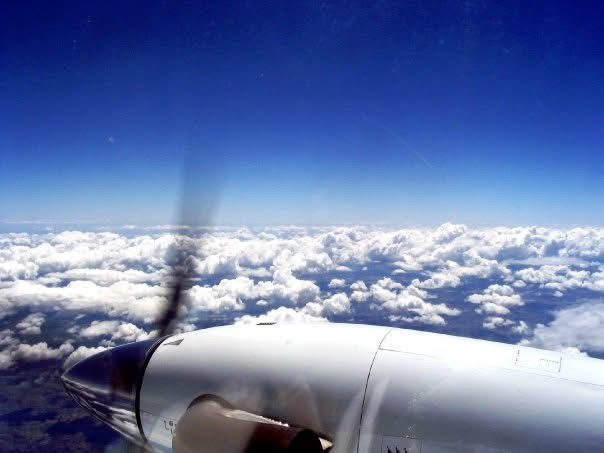A turboprop engine and spinning propeller above a bright layer of clouds