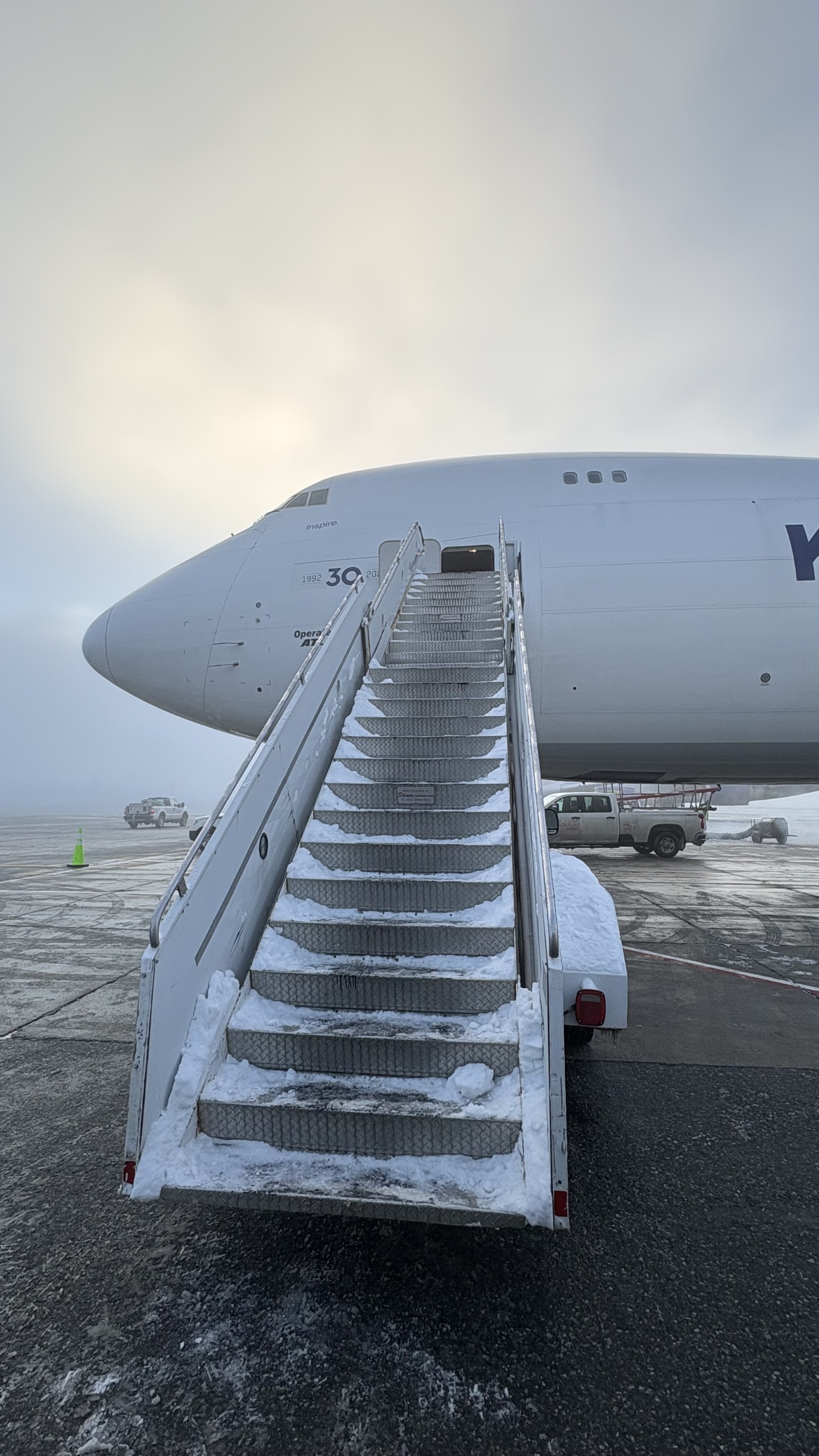 Snow-covered boarding stairs leading to a Boeing 747 on a misty winter apron