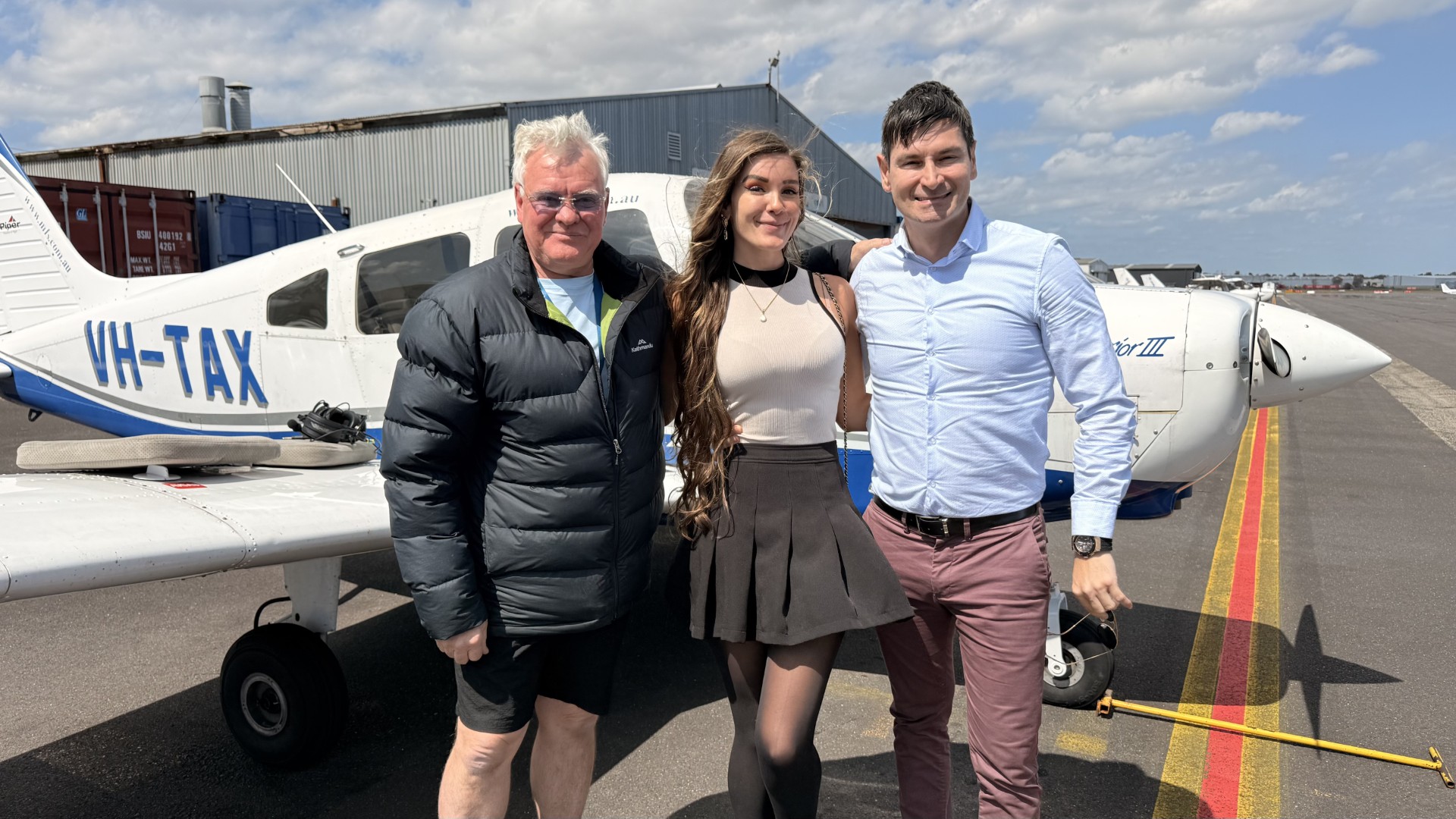 Three people standing together beside a light aircraft on the apron
