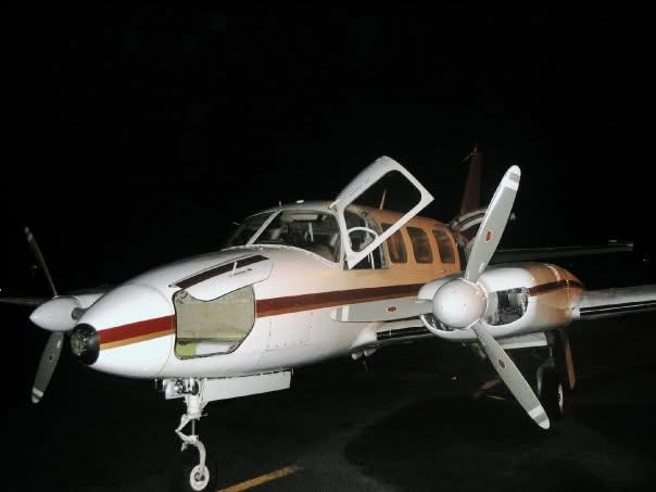 A twin-engine light aircraft with its doors open on a night apron