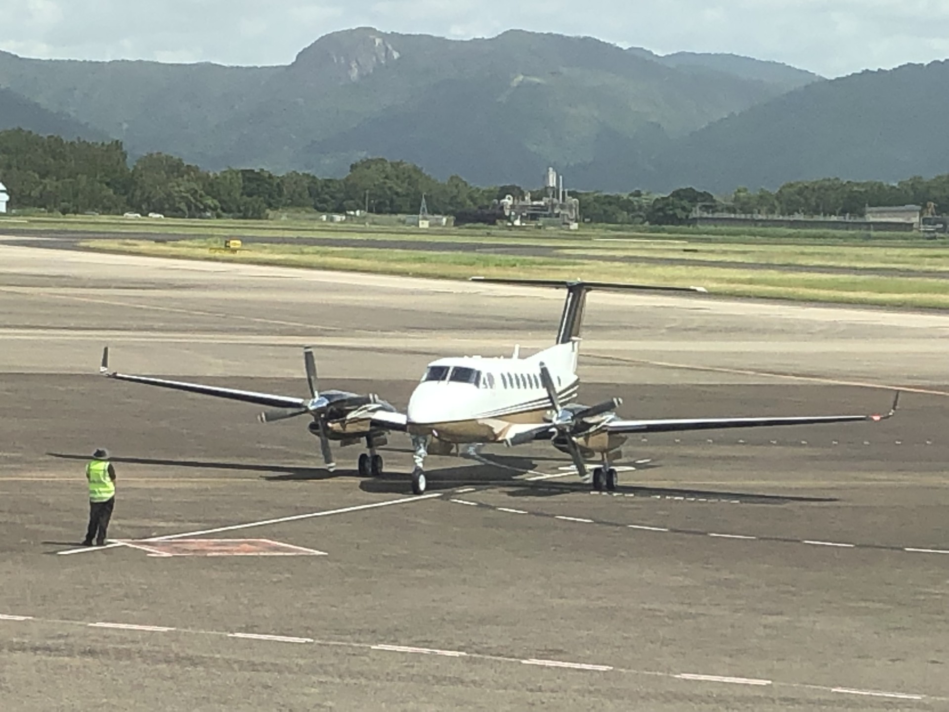 A twin turboprop and a ground marshaller on an apron beneath mountains
