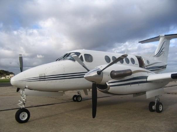 A white twin turboprop with dark blue stripes parked on the apron