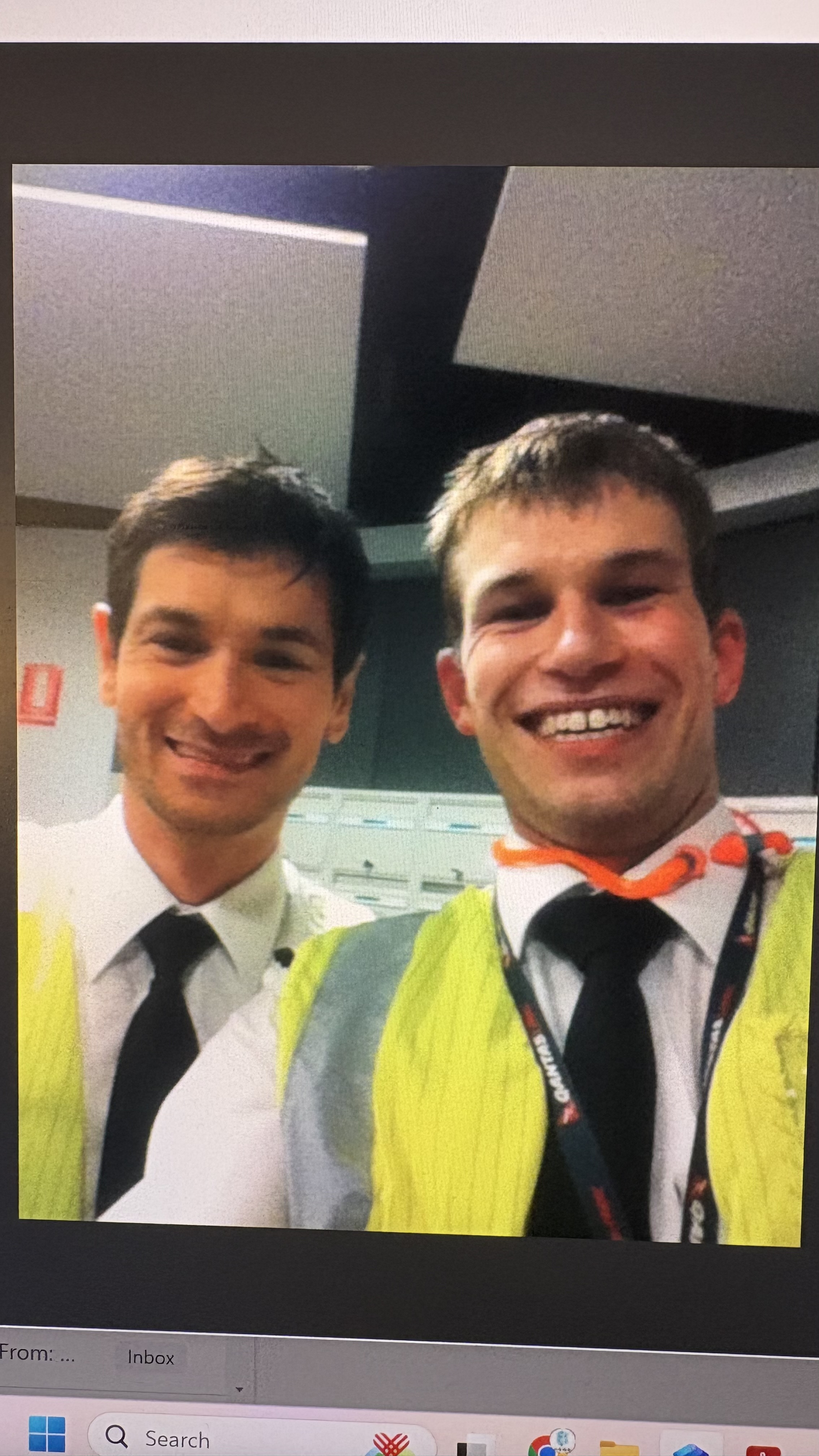 A photograph of two smiling pilots in uniform, one wearing a high-visibility vest