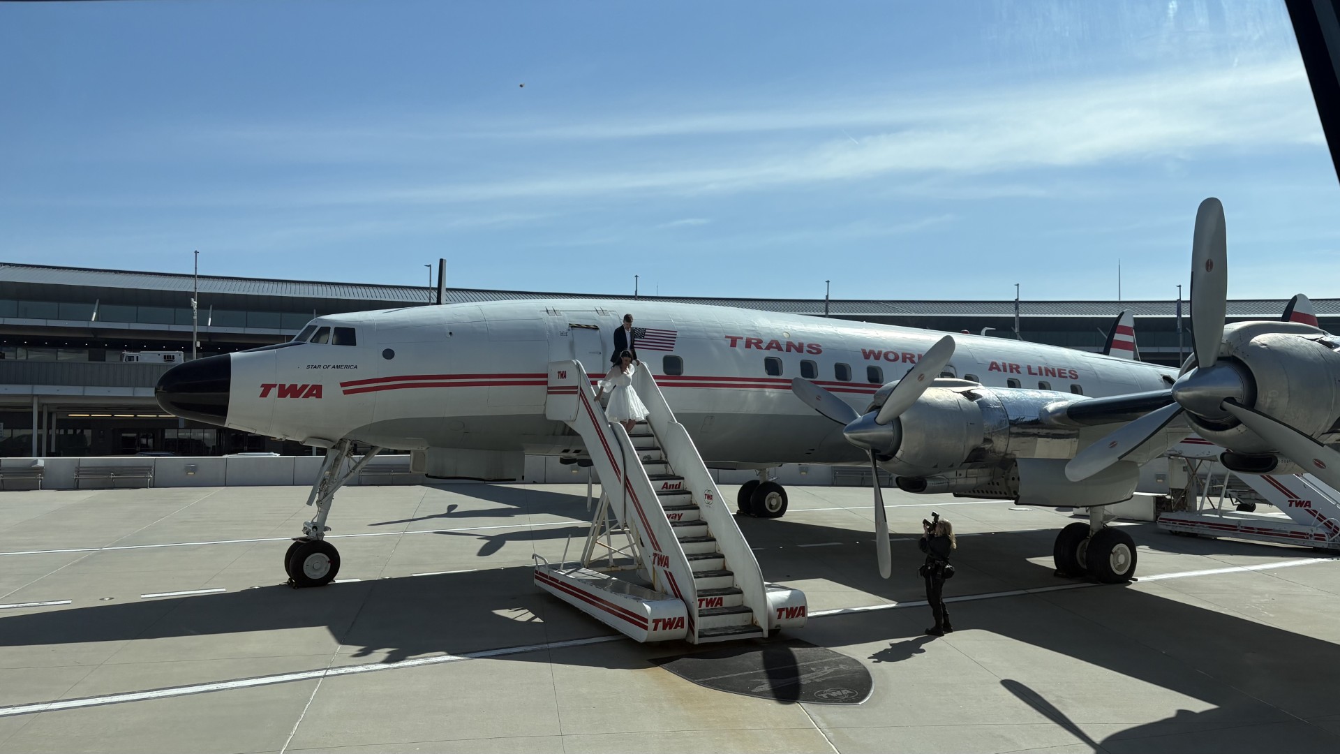 A vintage TWA propeller airliner with boarding stairs and visitors