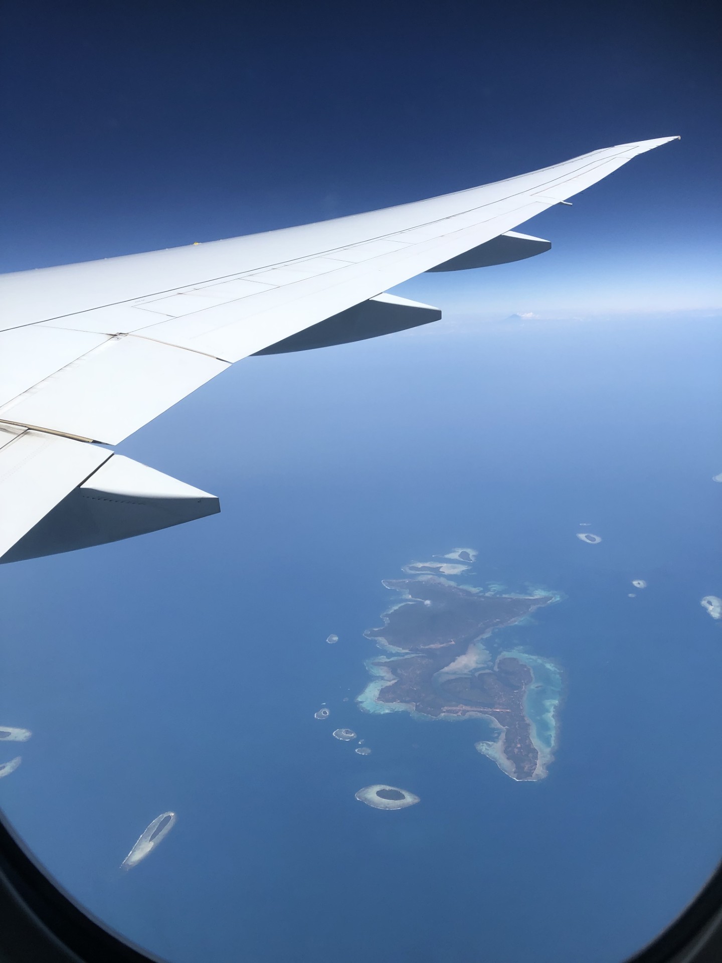 An airliner wing above islands and coral reefs in the ocean